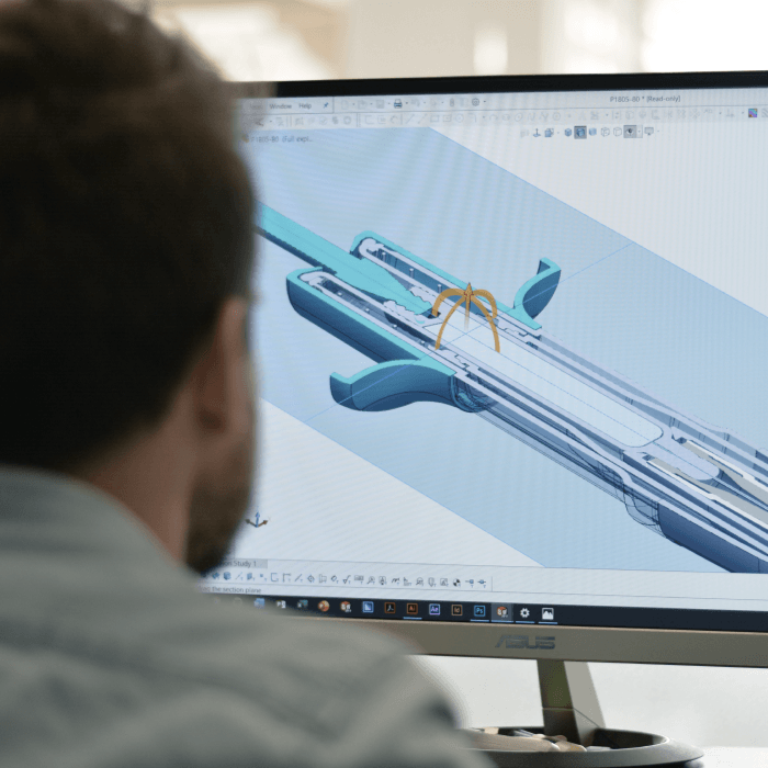 Image of a scientist viewing a computer screen with an engineering drawing of an auto injector pen displayed on the screen