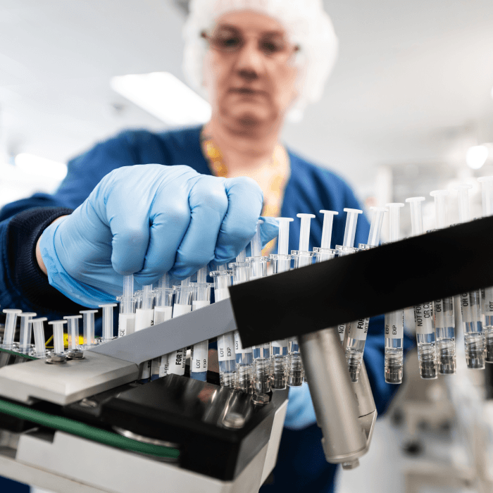 Image of a scientist grabbing syringes off of a filling line